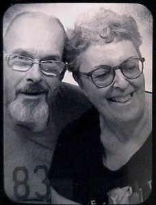 A vintage style, black and white photo of an older man and woman, both wearing glasses and looking very happy.
